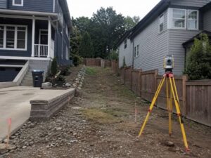 Survey equipment measuring boundaries and grade changes on a narrow residential infill lot between neighboring homes